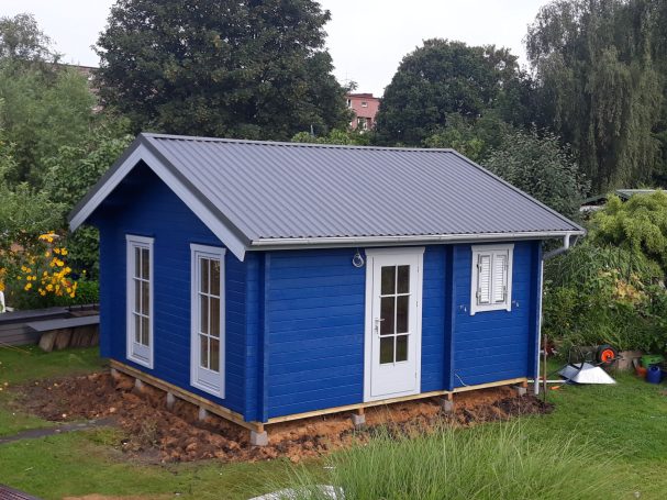 Blaue Gartenlaube mit weißer Tür und Fenster in grüner Umgebung.